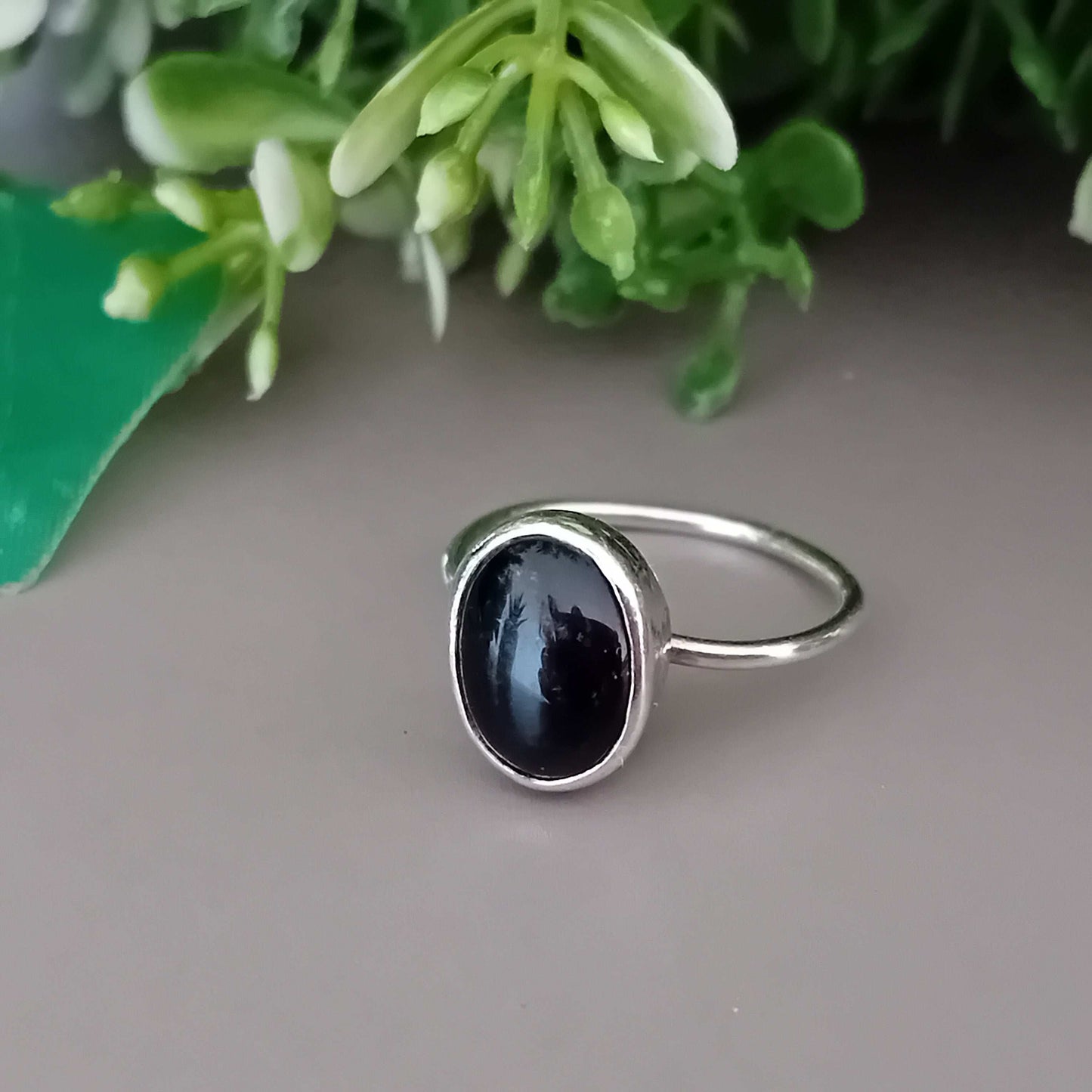 Sterling silver ring with a black onyx stone on a neutral background with greenery