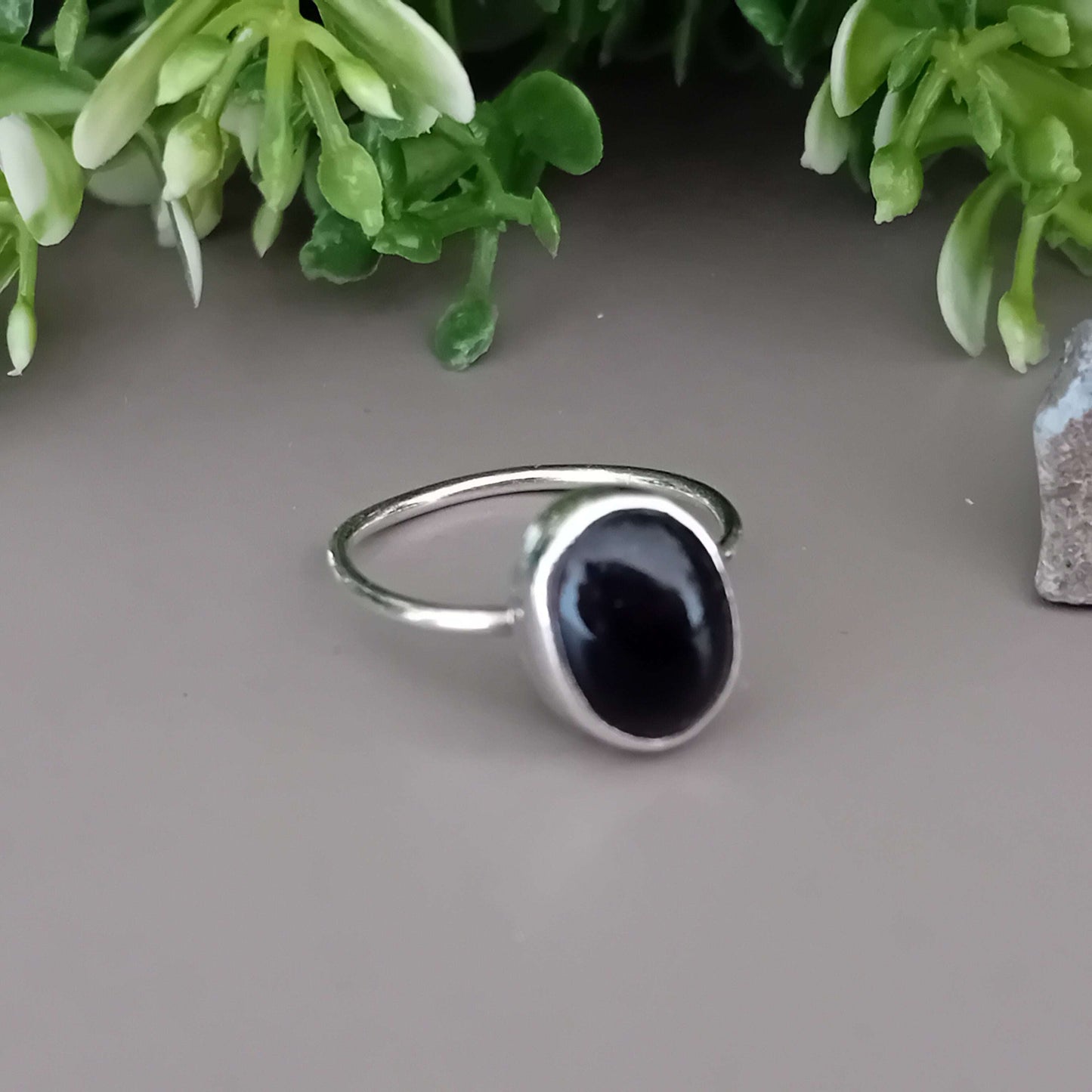Sterling silver ring with a black onyx gemstone on a gray surface with green foliage in the background