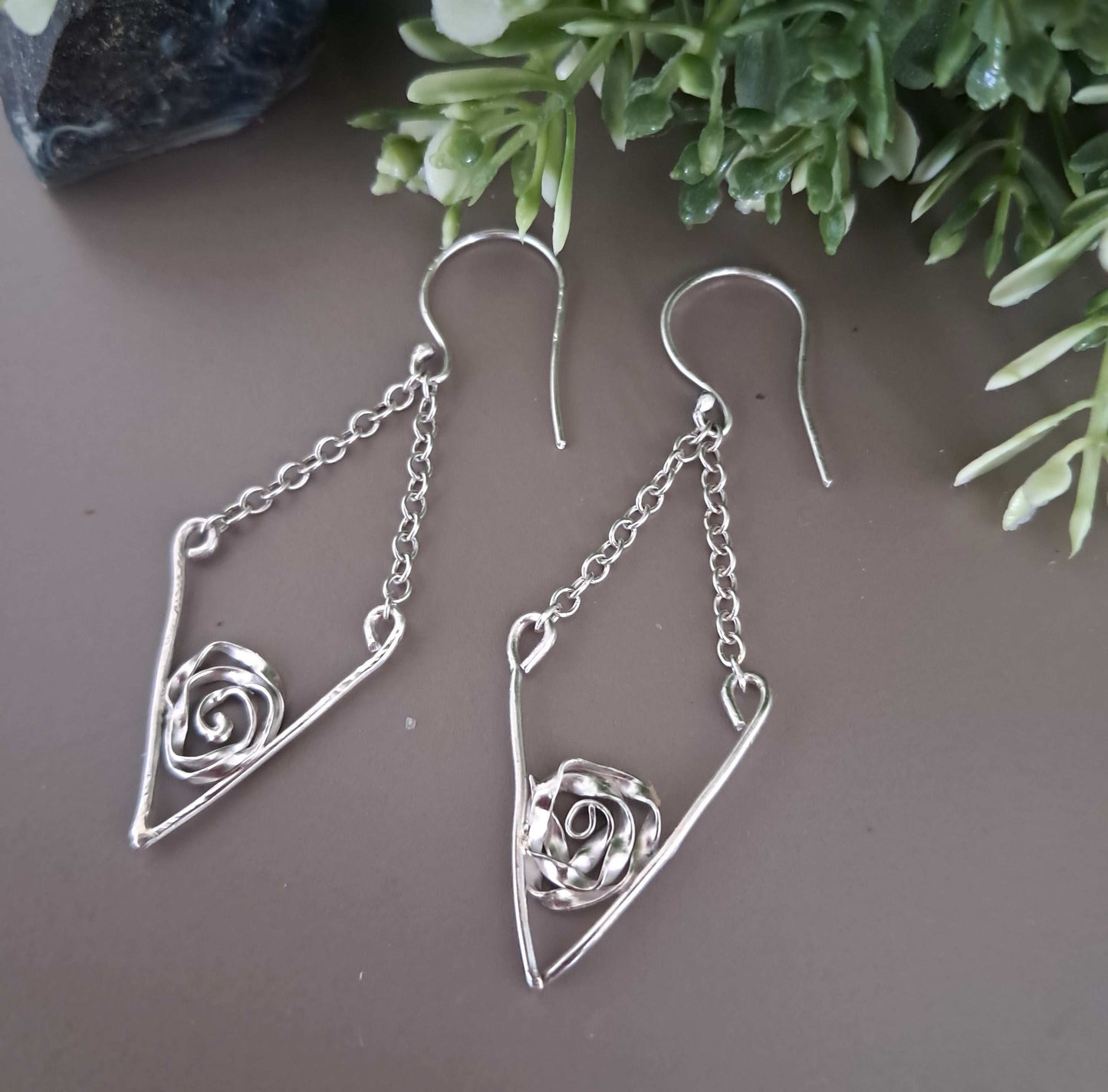 Handcrafted Sterling Silver Earrings with Rose Detail in Silver V with Chain Drop on Grey brown background with green leaves