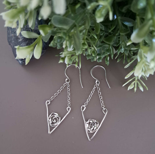 Sterling silver roses in silver V shape with chain drop on a gray surface with green foliage in the background