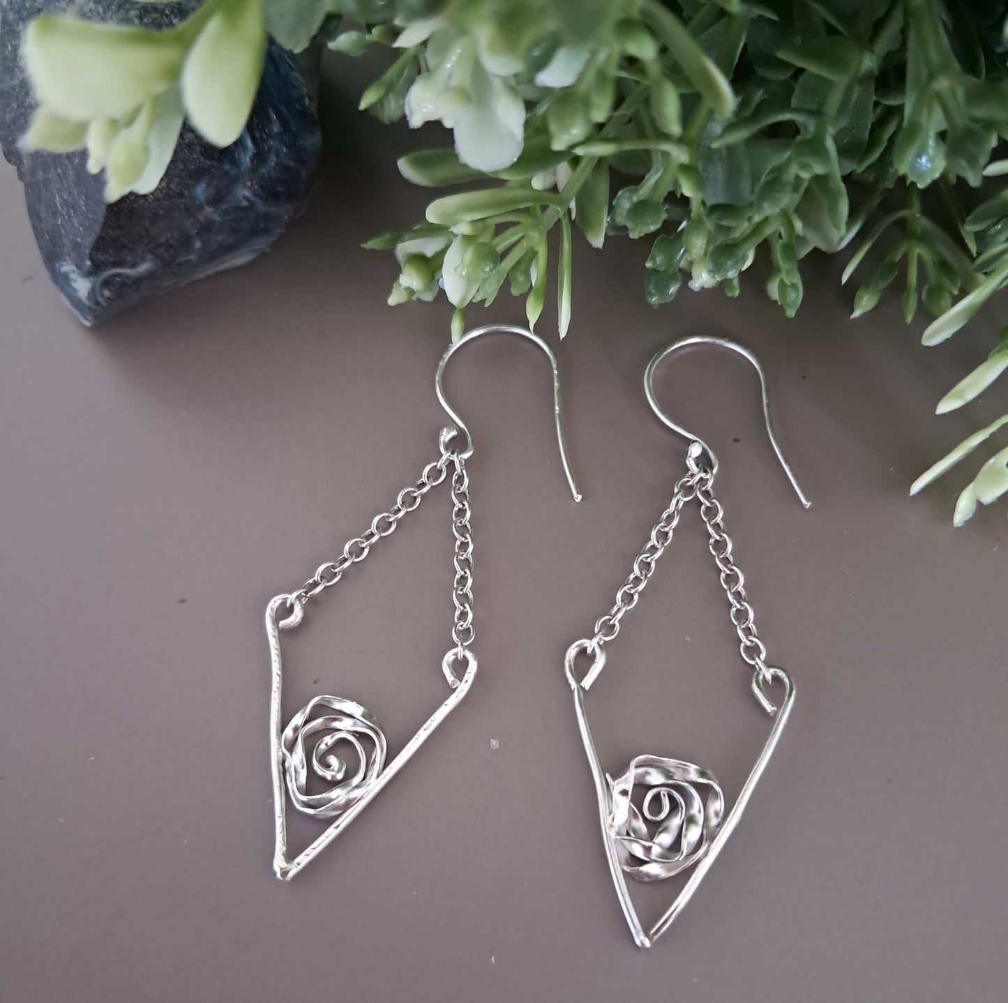 Sterling silver v shaped drop earrings with rose accents on a neutral background with greenery.