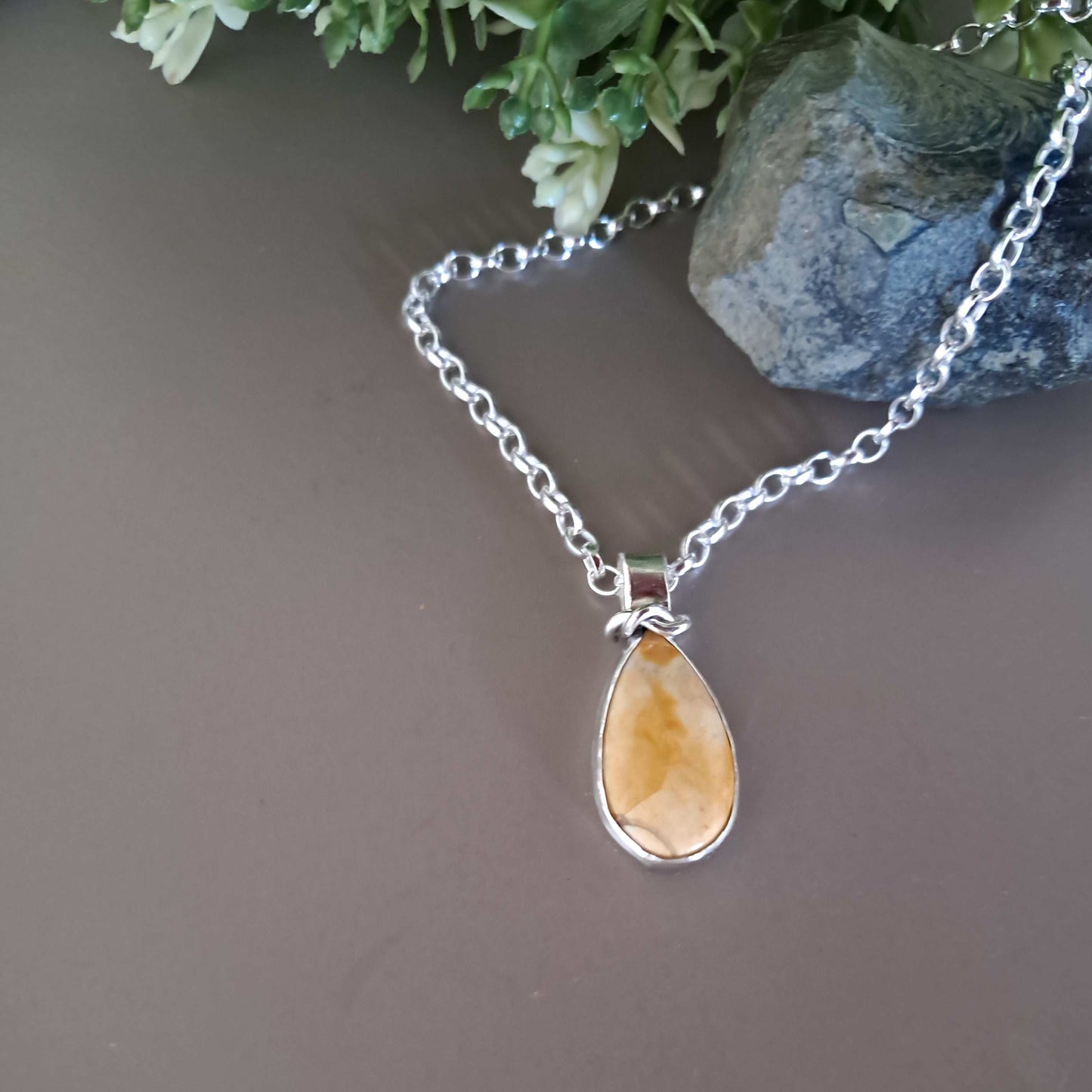 Handmade sterling silver bezel set jasper pendant on a silver chain with a natural background and green leaves