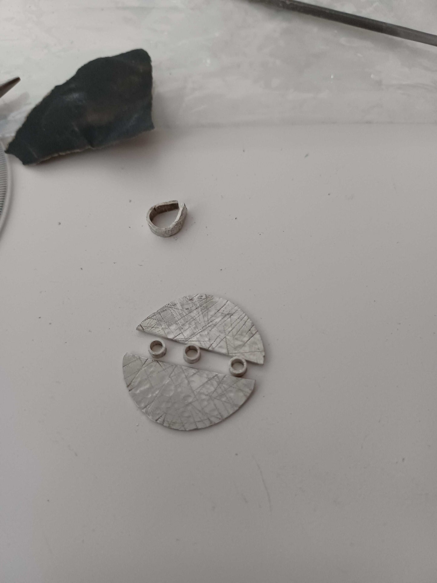 Silver semi circles with three circular tube objects being made into a necklace