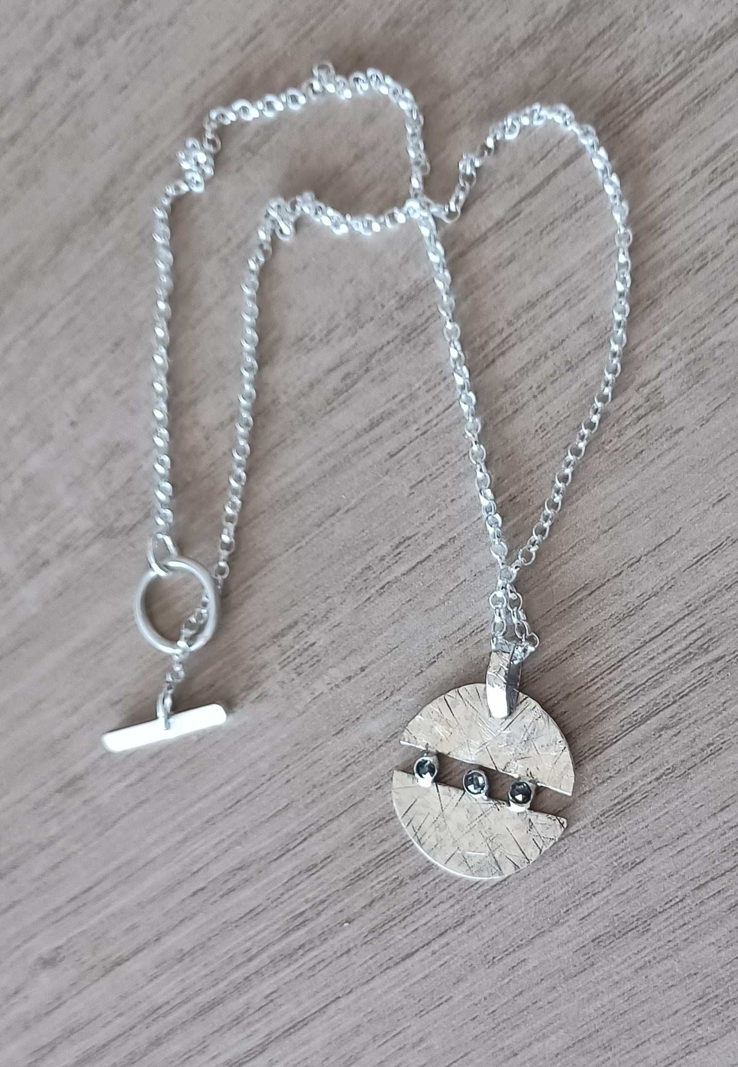 Handmade silver and diamond necklace in circular design with chunky chain on wooden background