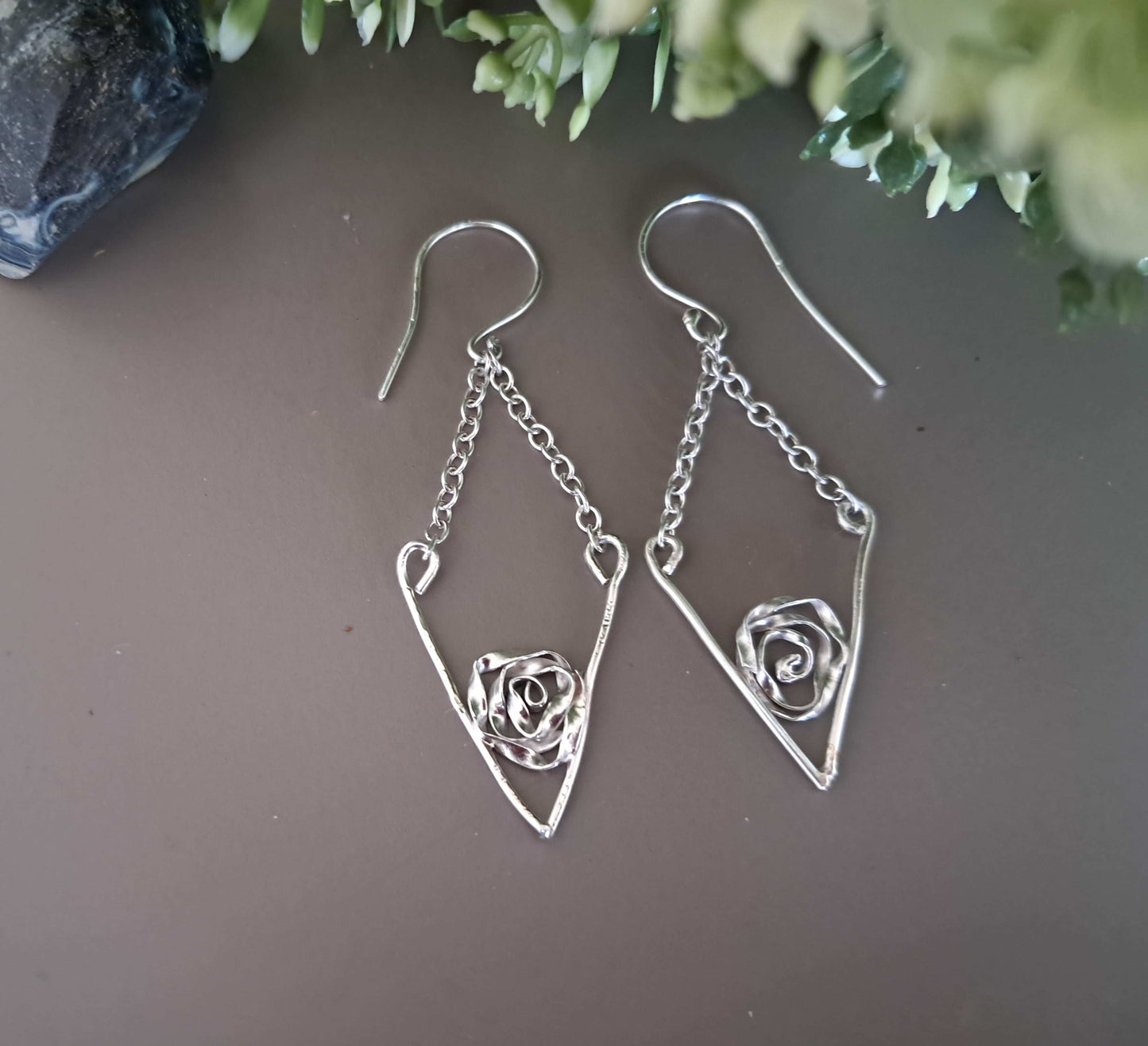Stering Silver V shape, chain drop, earrings with rose details on a brown surface with greenery.