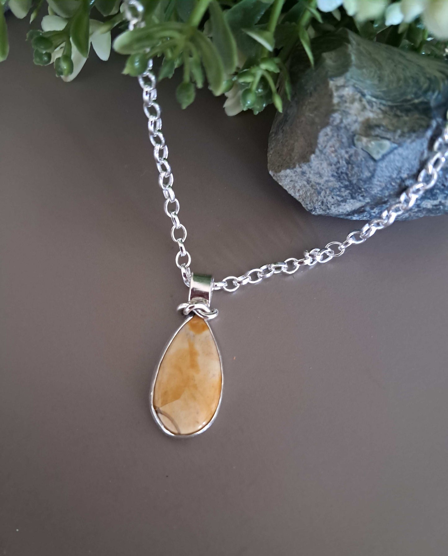 yellow jasper necklace with sterling silver bezel and decorative bail on neutral background with green foliage