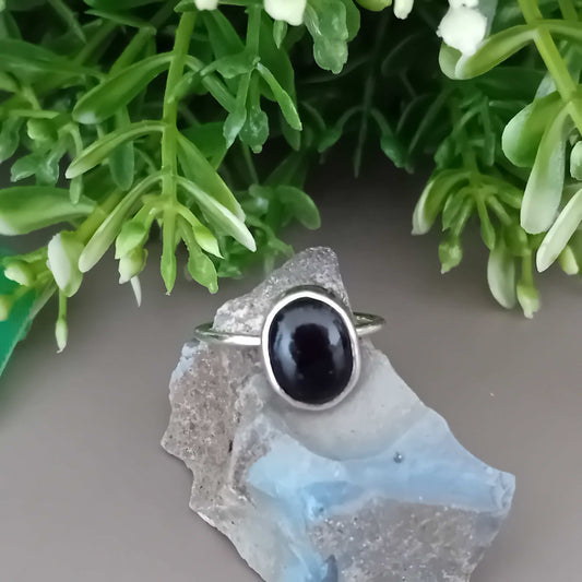 Sterling Silver Ring with a black onyx gemstone on a stone surface with green foliage in the background