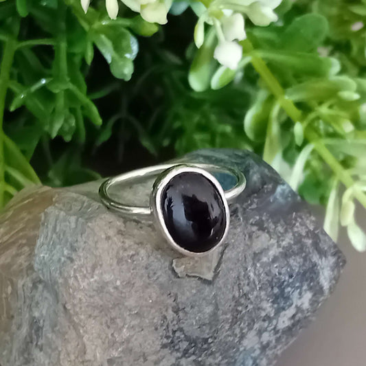 Sterling silver ring with a black onyx gemstone on a rock with greenery in the background