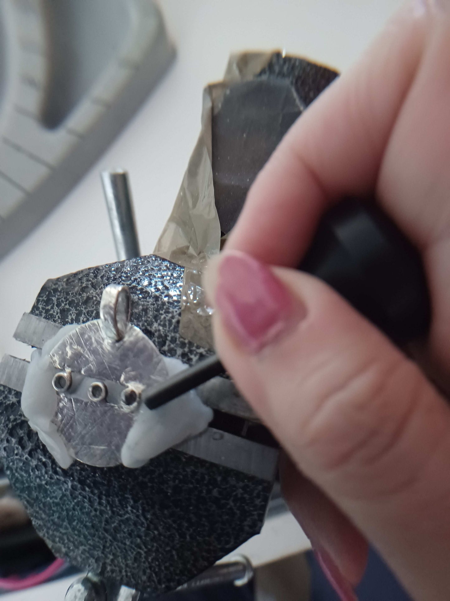 Close-up of a hand using a tool to make a silver pendant necklace being held in a bench vice 