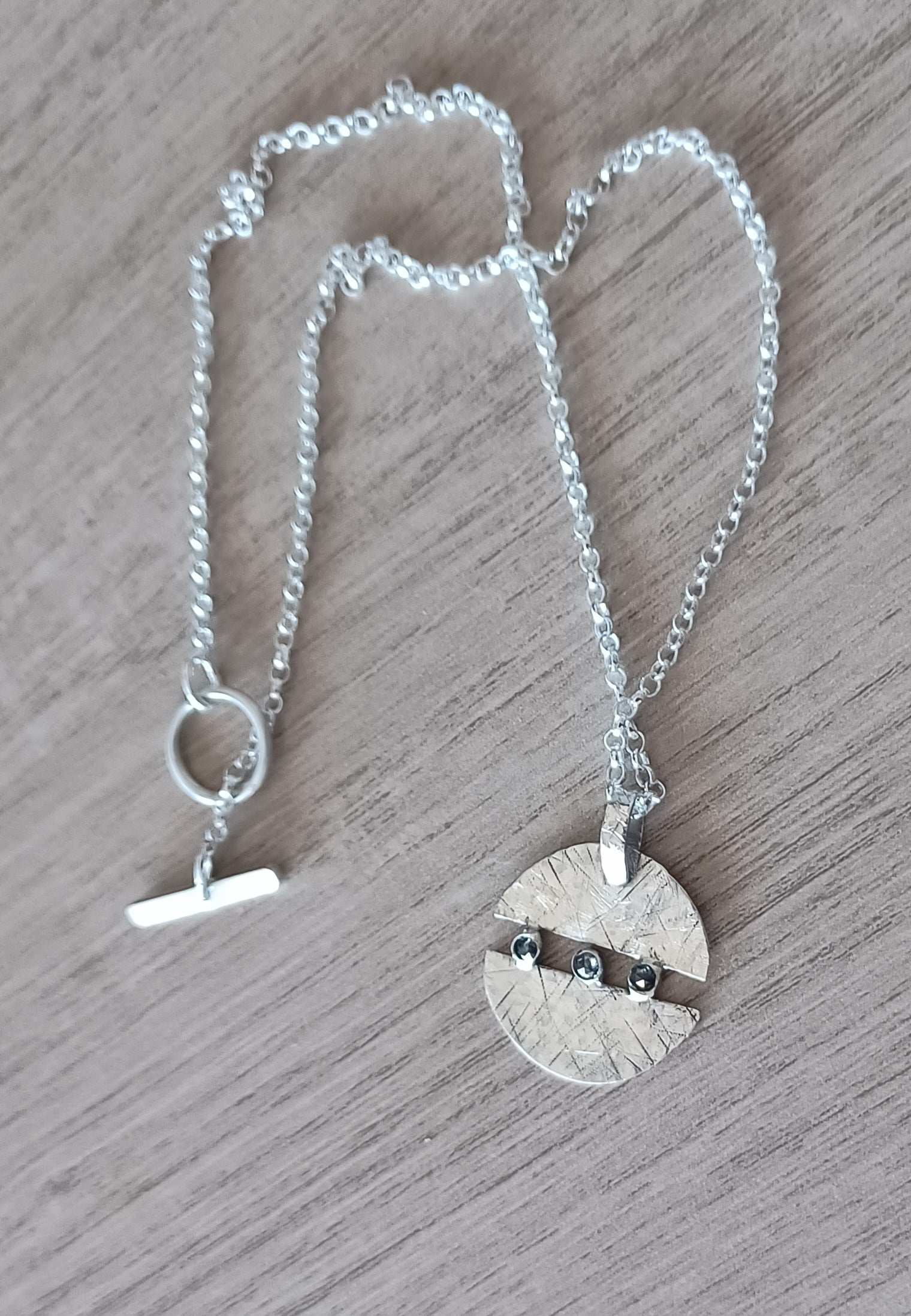 Handmade silver and diamond necklace in circular design with chunky chain on wooden background