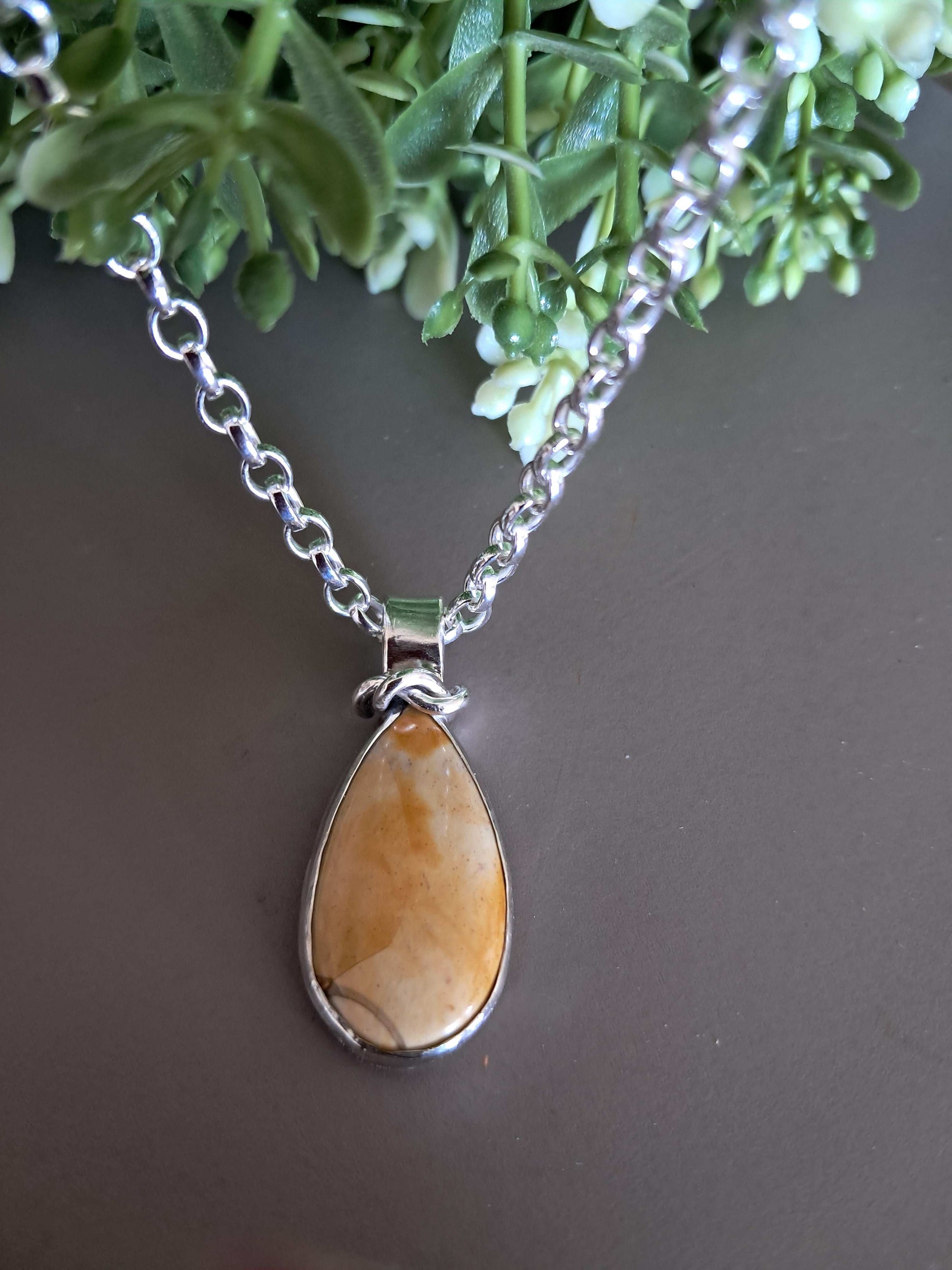 Necklace with a teardrop-shaped natural gemstone pendant on a neutral background with green foliage 
